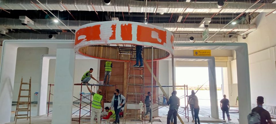 فريق عمل يبني هيكل جناح دائري على سقالات داخل القاعة
